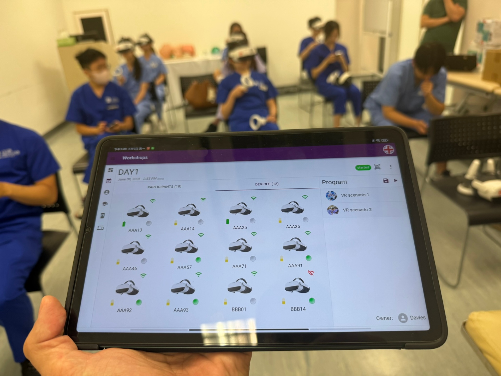 A facilitator holding a tablet showing the SimCloud console with twelve connected VR headsets during a workshop